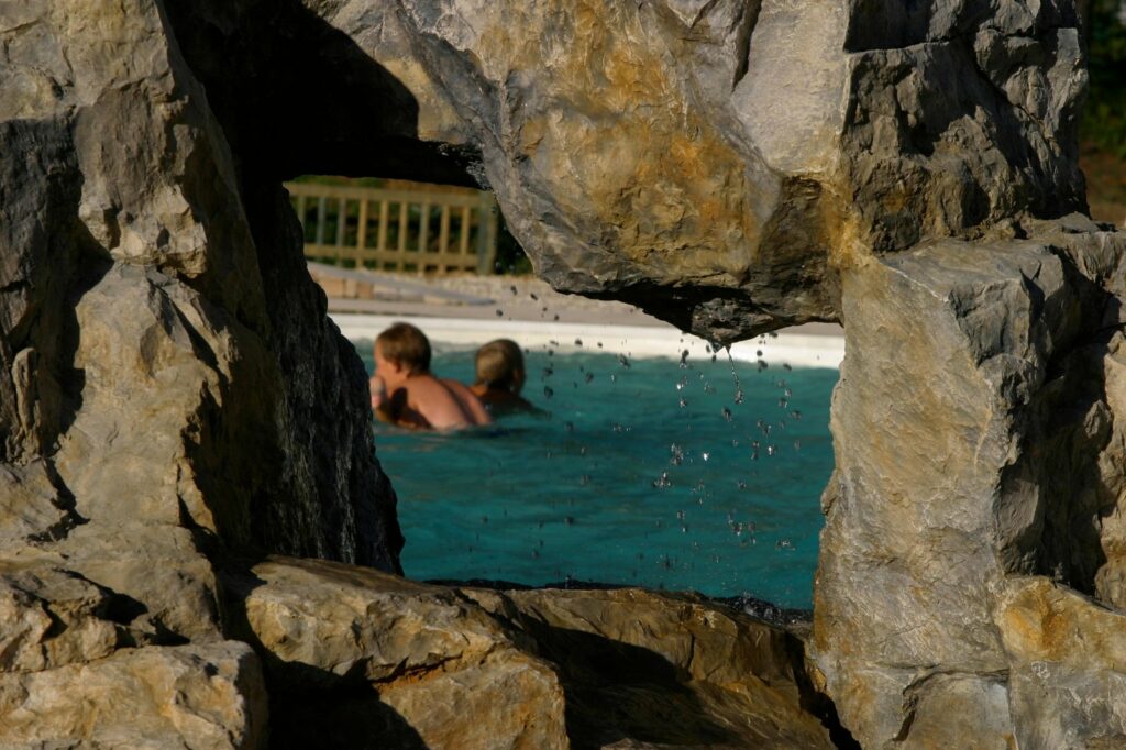 Ouverture dans une grotte en faux rocher avec des gouttes d'eau qui tombent devant une piscine